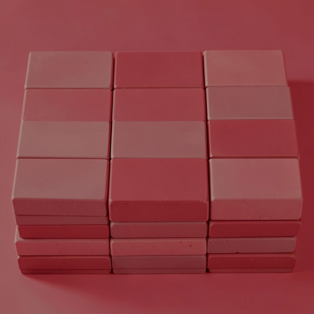 A duotone photograph in muted crimson and warm gray showing a stack of clean square tiles arranged in a balanced grid pattern.
